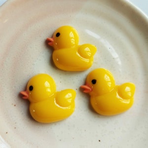 Puede incluir: Tres figuras de patos de goma amarillos en un plato blanco. Los patos tienen ojos negros y picos naranjas.