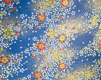 May include: A close-up of blue paper with a floral pattern. The design features white, red, green, and brown flowers, along with gold flecks. The flowers are scattered across the paper, creating a delicate and artistic look.