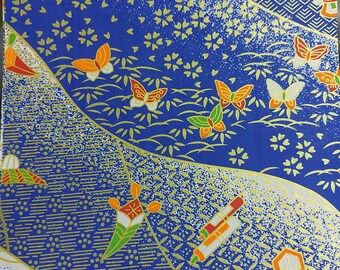 May include: Close-up of patterned paper with a blue backdrop. The design features gold accents, butterflies, and floral motifs. The paper has a textured appearance with a mix of geometric and organic shapes, creating a visually rich and detailed pattern.