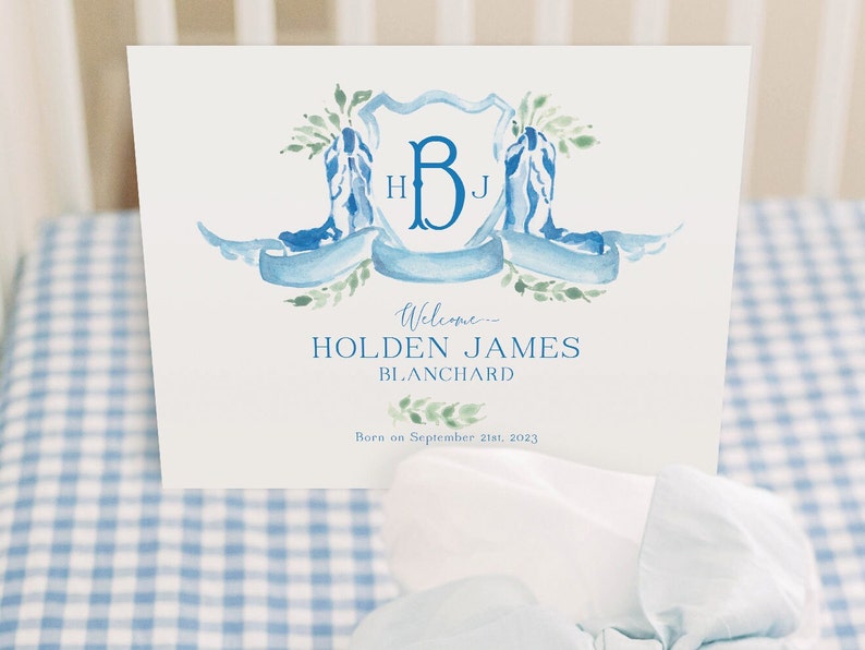 May include: A white card with a blue and green watercolor design featuring a monogram of the letters "H" and "B" with the letter "J" inside the "B". The text "Welcome Holden James Blanchard Born on September 21st, 2023" is printed below the monogram.