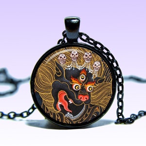 May include: Black necklace with a round pendant featuring a colorful illustration of a mythical creature with multiple eyes and skulls. The pendant is set in a black metal frame.