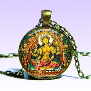 Puede incluir: Un collar de oro con un colgante redondo de vidrio que presenta una ilustración colorida de una deidad con múltiples brazos. La deidad está sentada en un trono con un halo y está rodeada de detalles intrincados.