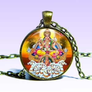 May include: A round glass pendant necklace with a bronze chain. The pendant features a colorful image of the Hindu deity Surya, the Sun God, riding a chariot pulled by seven white horses.