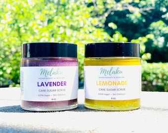 May include: Two 4-ounce jars of cane sugar scrub, one lavender and one lemonade. Both jars have black lids and white labels with the brand name "Melaku" and the scent name.