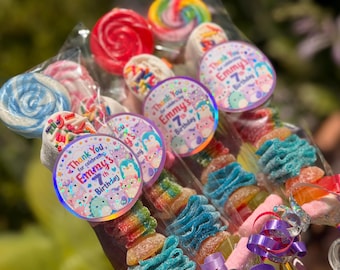 May include: A collection of candy skewers wrapped in clear plastic, featuring colorful gummy ribbons, marshmallows with sprinkles, and lollipops. Each skewer includes a round sticker that reads, Thank You for celebrating Emmy's 7th Birthday.
