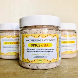 Pode incluir: Três frascos de vidro transparente cheios de um banho de imersão bege etiquetado como "Nourishing Bath Soak Spice Chai". O rótulo é amarelo com texto preto e indica que o produto é feito com minerais naturais da Terra e óleos essenciais terapêuticos para ajudar você a relaxar. Também indica que o produto é 100% vegano e livre de crueldade. Os frascos são de 4 oz cada um.