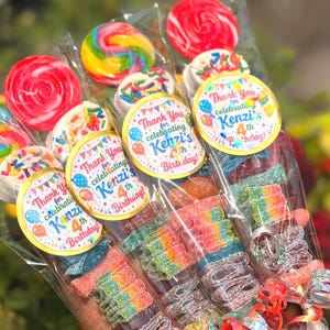 Könnte beinhalten: Mehrere durchsichtige Plastiktüten gefüllt mit bunten Süßigkeiten, darunter runde Lutscher, mit weißer Schokolade überzogene Stücke mit Streuseln und saure Regenbogenbänder. Jede Tüte hat einen runden Aufkleber mit der Aufschrift Thank You for celebrating Kenzi's 4th Birthday.