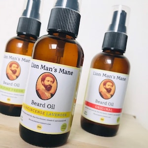 May include: Three amber glass bottles with black pump tops and white labels. The labels feature a man with a beard and the text "Lion Man's Mane Beard Oil". The bottles are labeled with different scents: "Alpine Fresh", "Frankincense Lavender", and "Original".