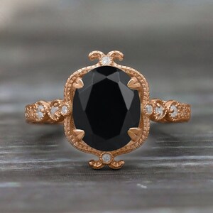 May include: A rose gold engagement ring with a black oval gemstone surrounded by smaller diamonds. The ring has a delicate, vintage-inspired design.