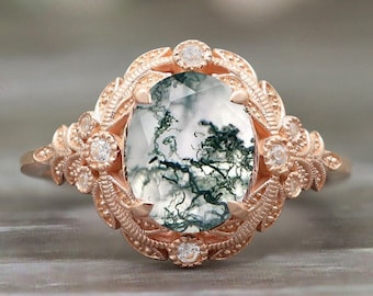 May include: A rose gold engagement ring with a large oval-shaped moss agate gemstone surrounded by smaller diamonds. The ring has a delicate floral design.