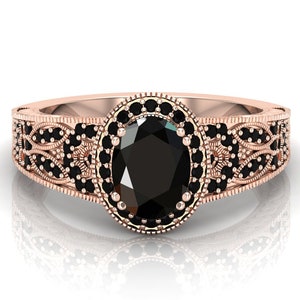 May include: A rose gold ring featuring an oval black gemstone set within a halo of smaller black gemstones. The band is adorned with a filigree design.