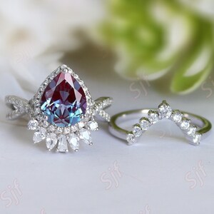 May include: A pear-shaped, iridescent gemstone ring with a halo of smaller diamonds. The ring is set in silver and has a matching curved band with diamonds.