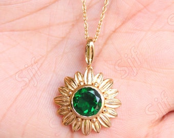 May include: A gold necklace with a green gemstone sunflower pendant. The pendant has a round green gemstone in the center surrounded by gold petals.