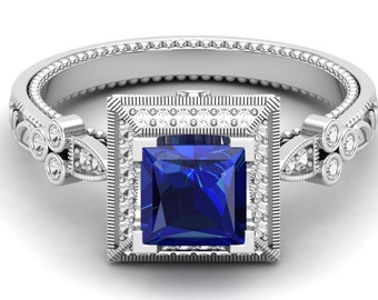 May include: A silver ring with a square blue sapphire gemstone surrounded by smaller diamonds. The ring has a decorative band with a beaded design.