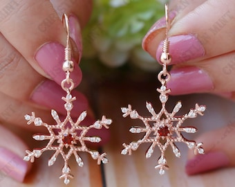 May include: Rose gold snowflake earrings with clear and red cubic zirconia stones.