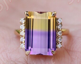 May include: A gold ring with a large, rectangular, multi-colored gemstone. The gemstone is yellow at the top, fading to purple at the bottom. The ring is set with small, clear diamonds around the gemstone.