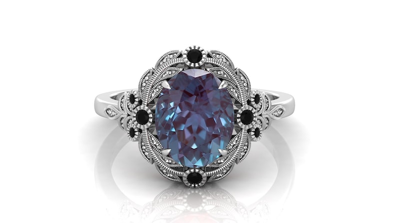 Puede incluir: Anillo de plata con una piedra preciosa de alejandrita de talla ovalada que cambia de color. El anillo presenta un engaste decorativo con detalles en negro y un dise&ntilde;o de filigrana detallado.