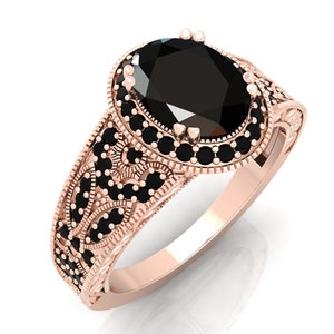 May include: A rose gold ring featuring a large oval black gemstone encircled by smaller black gemstones. The band is intricately designed with a floral pattern.