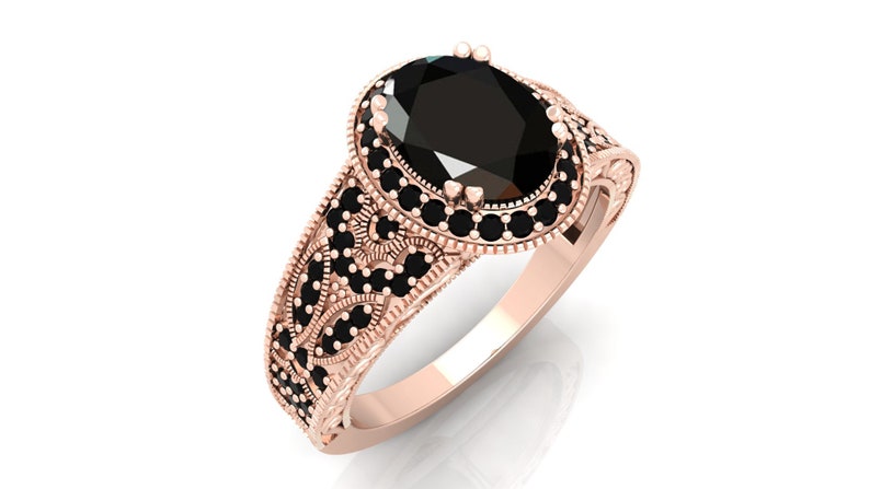 May include: A rose gold ring featuring a large oval black gemstone encircled by smaller black gemstones. The band is intricately designed with a floral pattern.