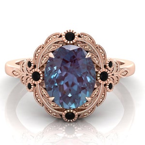 Puede incluir: Anillo de oro rosa con una piedra preciosa de alejandrita ovalada que cambia de color. El anillo presenta un dise&ntilde;o floral detallado con detalles en negro. La banda tiene un patr&oacute;n de filigrana ornamentado.