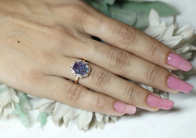 May include: A rose gold ring with a large oval-shaped purple gemstone surrounded by smaller white gemstones.
