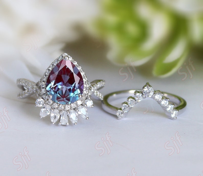 May include: A pear-shaped, iridescent gemstone ring with a halo of smaller diamonds. The ring is set in silver and has a matching curved band with diamonds.