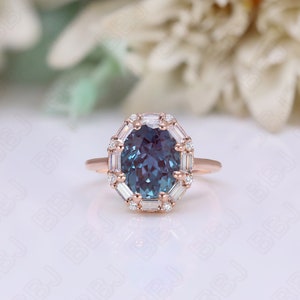 May include: A rose gold engagement ring with a large oval-shaped blue gemstone surrounded by a halo of smaller white gemstones.