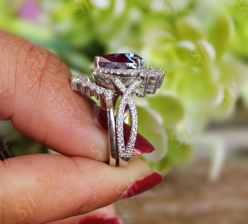 May include: A silver ring set with a large, oval-shaped, red gemstone surrounded by smaller, clear gemstones. The ring is set on a band with a twisted design and a smaller band with a row of clear gemstones.