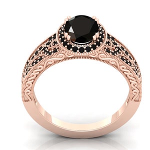 May include: A rose gold engagement ring featuring a black diamond centre stone and a halo of smaller black diamonds. The band is decorated with intricate scrollwork.