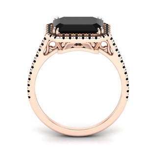 Op de afbeelding: Ros&eacute;gouden ring met een grote, rechthoekige zwarte edelsteen. De edelsteen is omgeven door een halo van kleinere zwarte stenen. De band is ros&eacute;goud met zwarte accenten, wat een opvallend contrast cre&euml;ert. Het ontwerp van de ring is elegant.