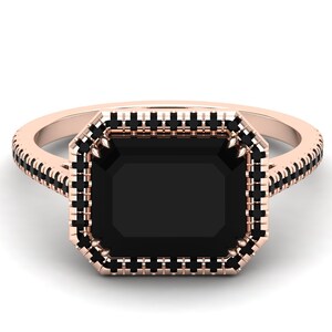 Op de afbeelding: Ros&eacute;gouden ring met een grote, rechthoekige zwarte edelsteen. De edelsteen is omgeven door een halo van kleinere zwarte stenen, met extra zwarte stenen langs de band. De ring heeft een klassiek, elegant ontwerp.
