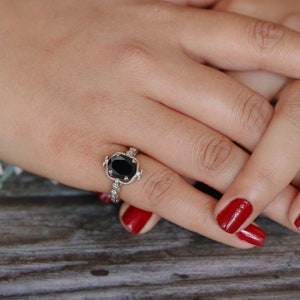May include: A silver ring with a large black oval gemstone surrounded by smaller white gemstones. The ring is on a finger with red nail polish.