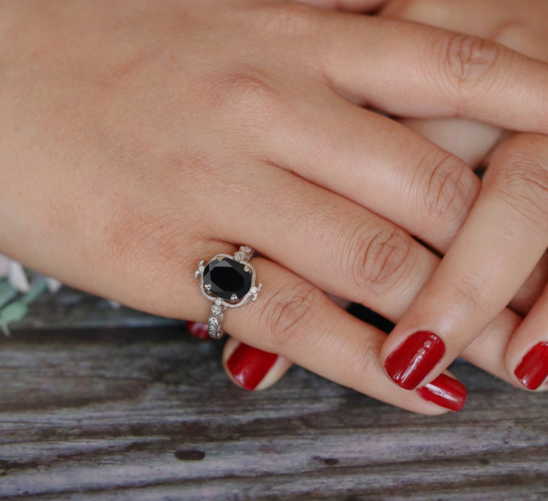 May include: A silver ring with a large black oval gemstone surrounded by smaller white gemstones. The ring is on a finger with red nail polish.
