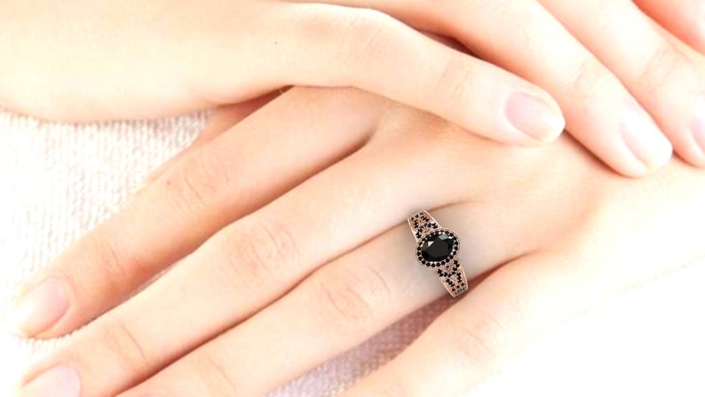 May include: A rose gold ring featuring a black oval gemstone surrounded by smaller black gemstones. The ring is worn on a finger.