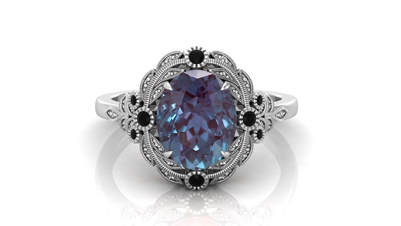 Puede incluir: Anillo de plata con una gema de alejandrita ovalada. El anillo presenta un engaste decorativo con detalles en negro. La gema est&aacute; rodeada por un dise&ntilde;o de filigrana detallado.