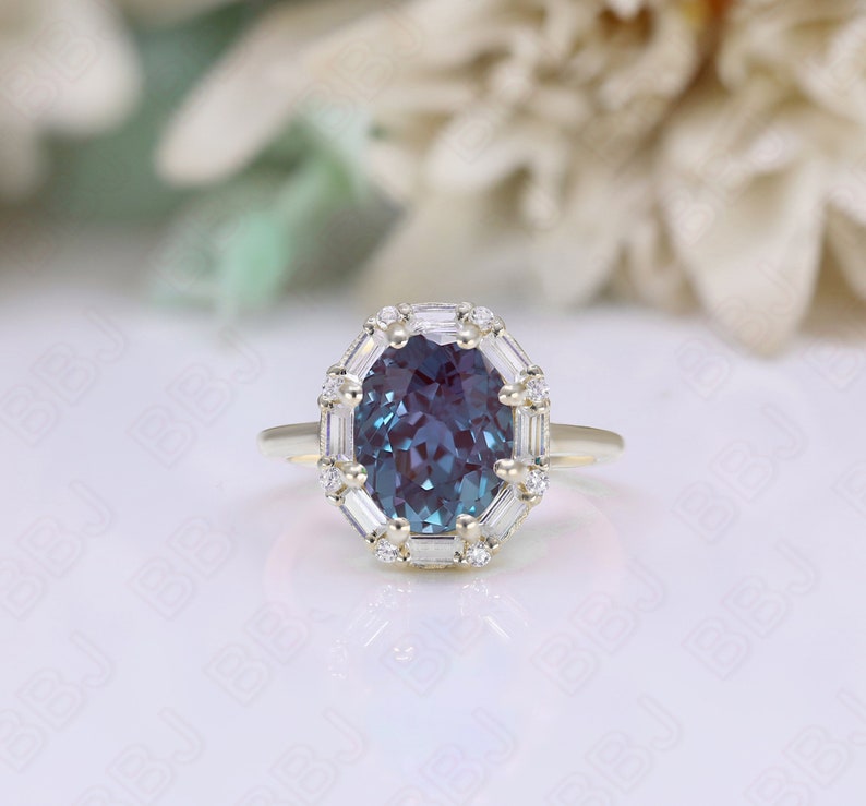 May include: A gold ring with a large oval-shaped blue gemstone surrounded by a halo of smaller diamonds. The ring is set on a white background.