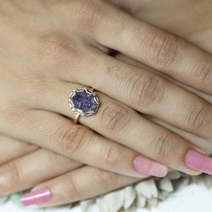May include: A rose gold ring with a large oval-shaped purple gemstone surrounded by smaller clear gemstones.