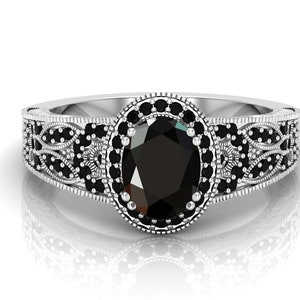 May include: A silver ring featuring an oval black gemstone encircled by smaller black gemstones. The ring boasts a delicate filigree design.