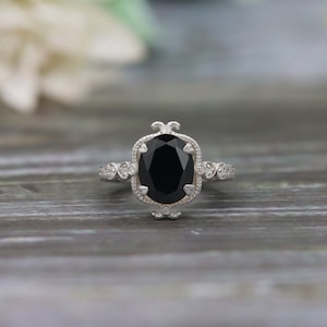 May include: A silver ring with a large black oval gemstone surrounded by smaller white gemstones. The ring has a delicate, ornate design.