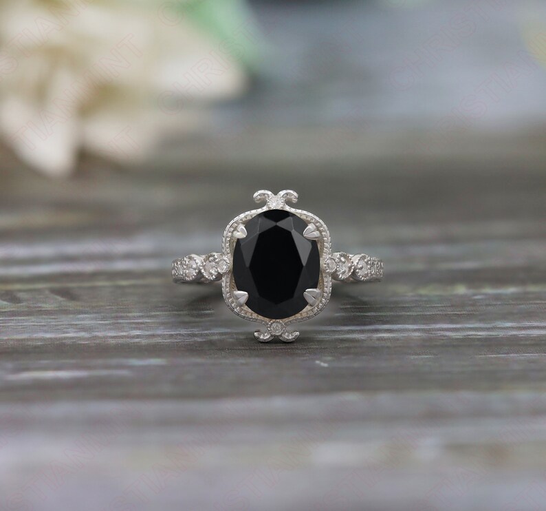 May include: A silver ring with a large black oval gemstone surrounded by smaller white gemstones. The ring has a delicate, ornate design.