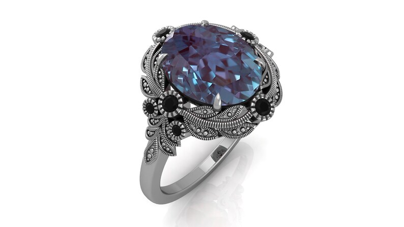 Puede incluir: Anillo de plata con una gema ovalada en tonos azules y morados. El anillo presenta detalles de filigrana floral y de hojas, acentuados con gemas negras. Un dise&ntilde;o cl&aacute;sico y elegante, ideal para ocasiones especiales.