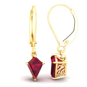 May include: A pair of gold-colored leverback earrings. One earring features a red, diamond-shaped gemstone, while the other has a rectangular red gemstone with gold filigree detailing. The earrings are set against a white background.