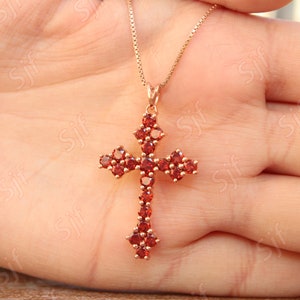 May include: A gold chain necklace with a red gemstone cross pendant. The cross is made of small, round red gemstones.