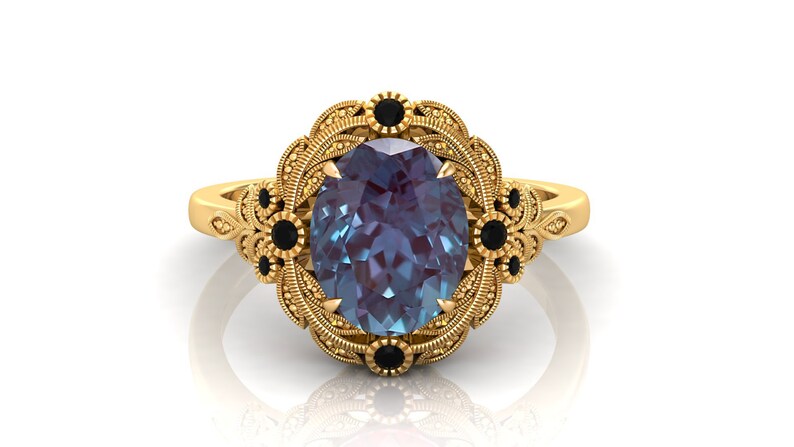 Puede incluir: Anillo dorado con una piedra preciosa ovalada de color azul-p&uacute;rpura. El anillo presenta un dise&ntilde;o floral ornamentado con detalles negros. La banda y el engaste est&aacute;n decorados con intrincados patrones.