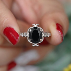 May include: A silver ring with a large oval black gemstone set in a filigree design. The ring is surrounded by smaller diamonds.