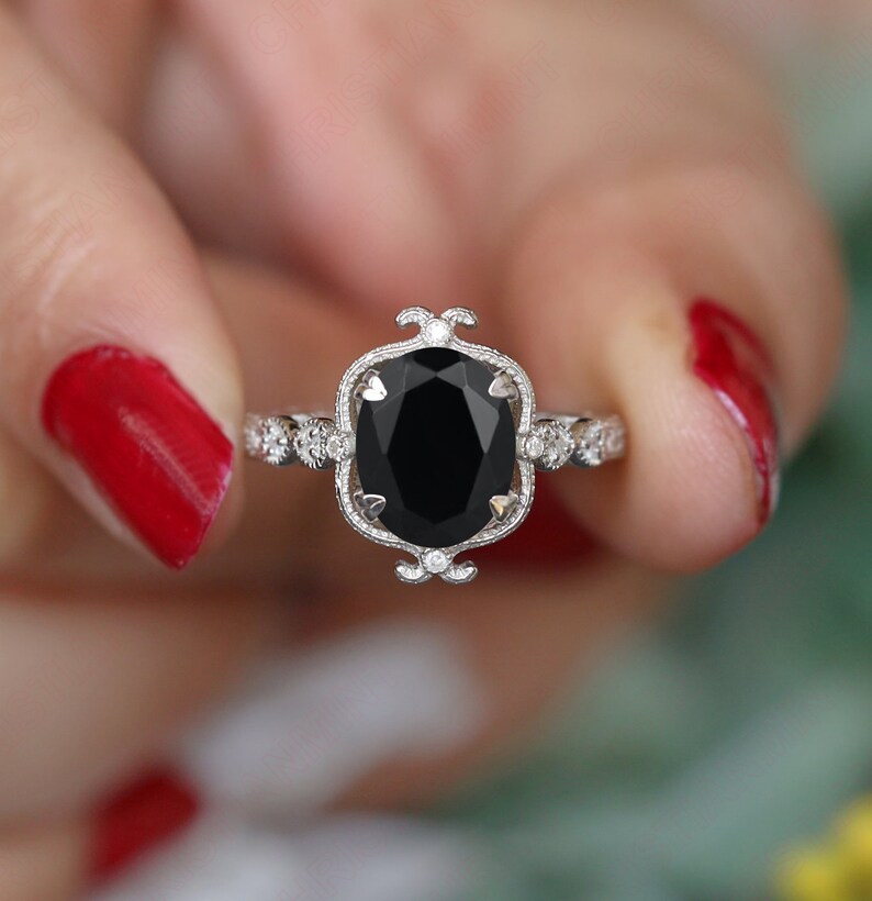May include: A silver ring with a large oval black gemstone set in a filigree design. The ring is surrounded by smaller diamonds.