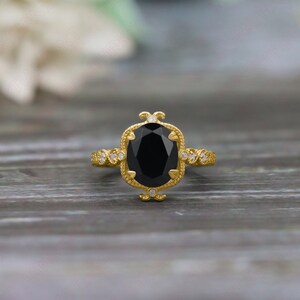 May include: A gold ring with a large oval black onyx gemstone surrounded by smaller diamonds. The ring has a delicate, ornate design.