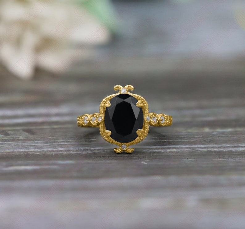 May include: A gold ring with a large oval black onyx gemstone surrounded by smaller diamonds. The ring has a delicate, ornate design.