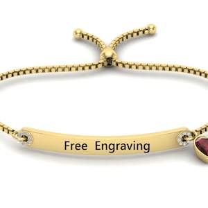 Puede incluir: Un brazalete ajustable de oro con un dije en forma de corazón y una barra que dice "Grabado gratis".