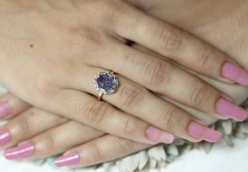 May include: A rose gold ring with a large oval-shaped purple gemstone surrounded by smaller clear gemstones.
